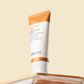 A squeeze tube of SKINEVER Salicylic Acid Peeling Scrub with white and orange packaging, standing upright on a reflective metallic surface against a solid beige background.