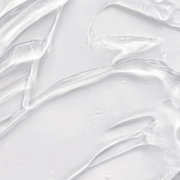 A close-up texture shot of a thick, clear, gel-like cosmetic cream or serum swirled on a light gray-white surface.
