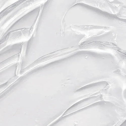 A close-up texture shot of a thick, clear, gel-like cosmetic cream or serum swirled on a light gray-white surface.