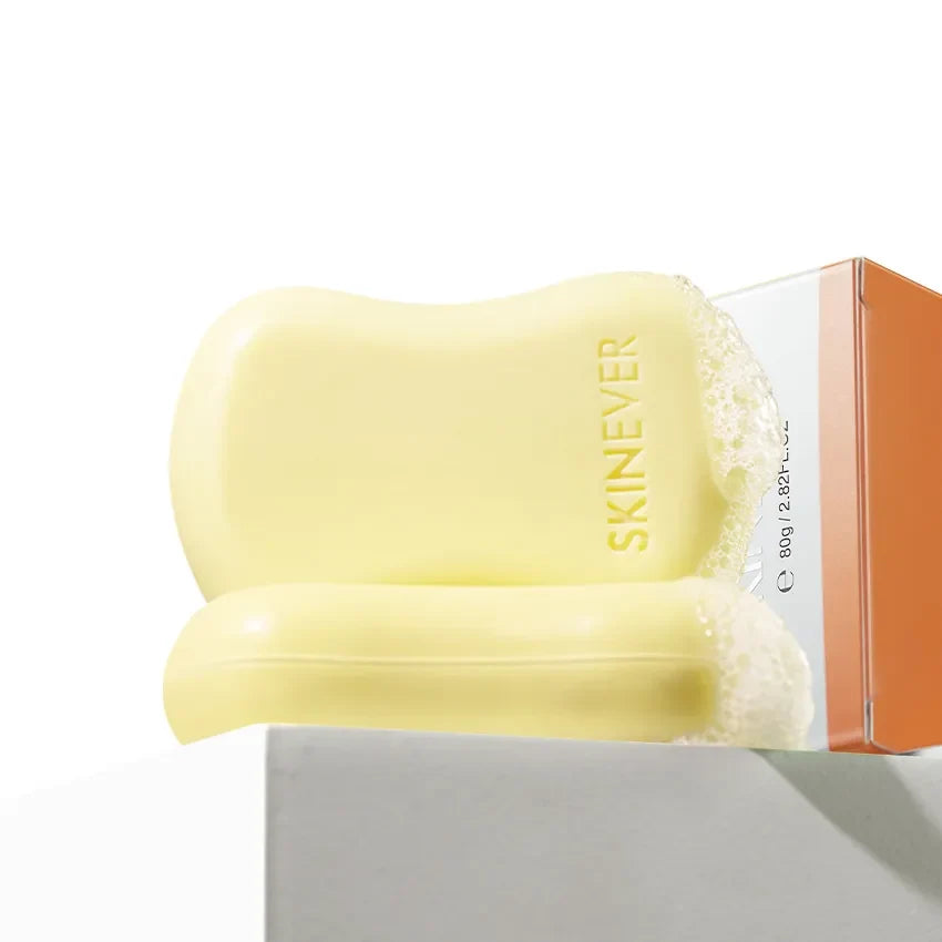A pale yellow SKINEVER soap bar with a matching bar resting in front, partially covered in foam, shown next to its orange and white packaging box on a white background.