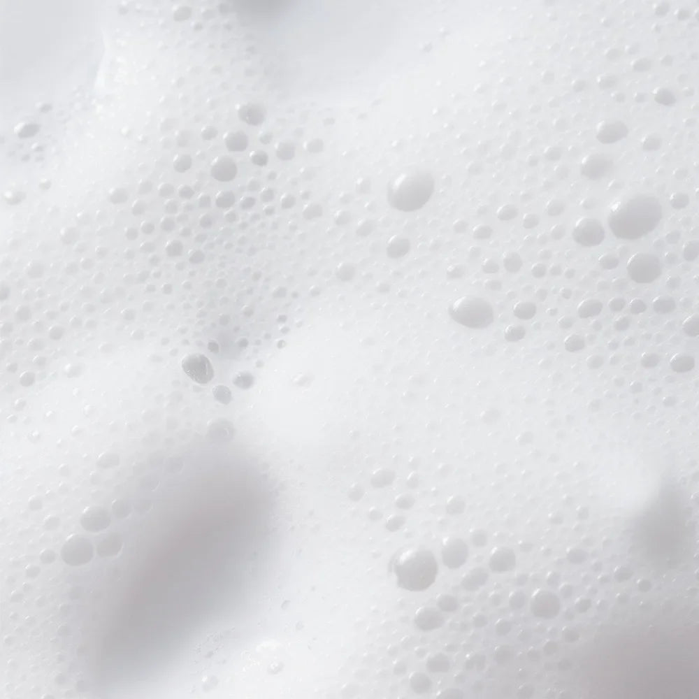 A close-up texture shot of white lathered foam with numerous small bubbles and soft shadows.