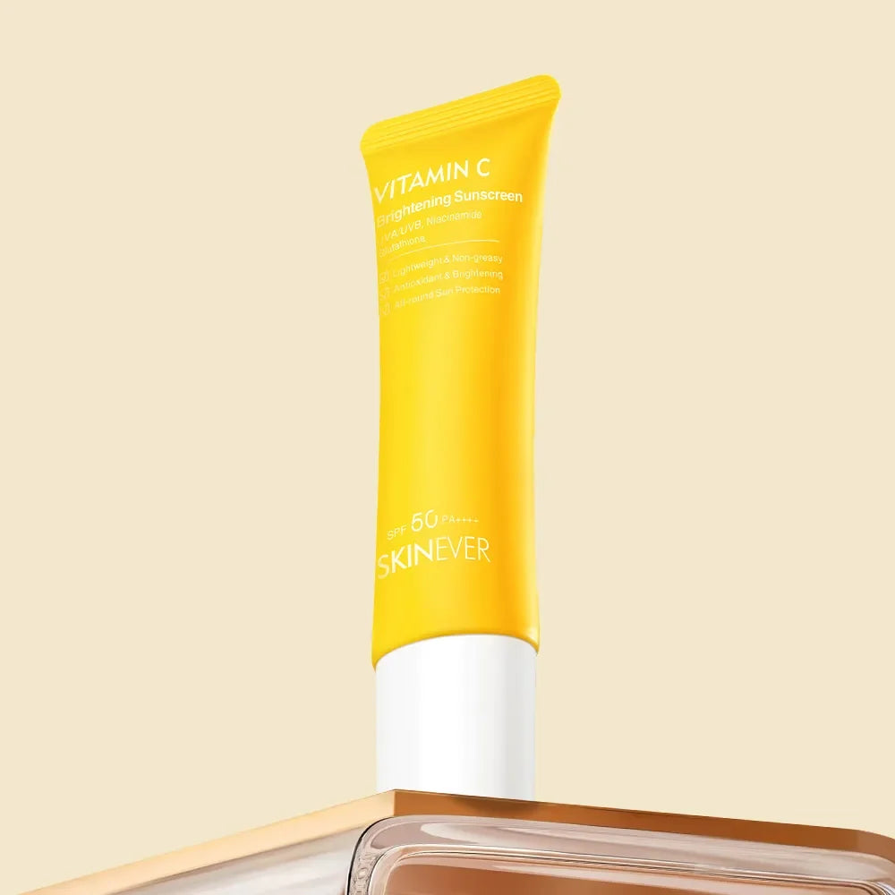 A yellow squeeze tube of SKINEVER Vitamin C Firming Sunscreen SPF 50+ with a white cap, standing upright on a reflective surface against a solid beige background.