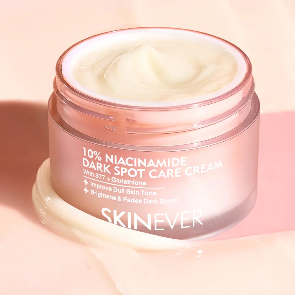 SKINEVER 10% Niacinamide Dark Spot Care Cream in a clear jar with a pink lid, showing the white cream inside, set against a soft pink background with a smear of the cream in the foreground.