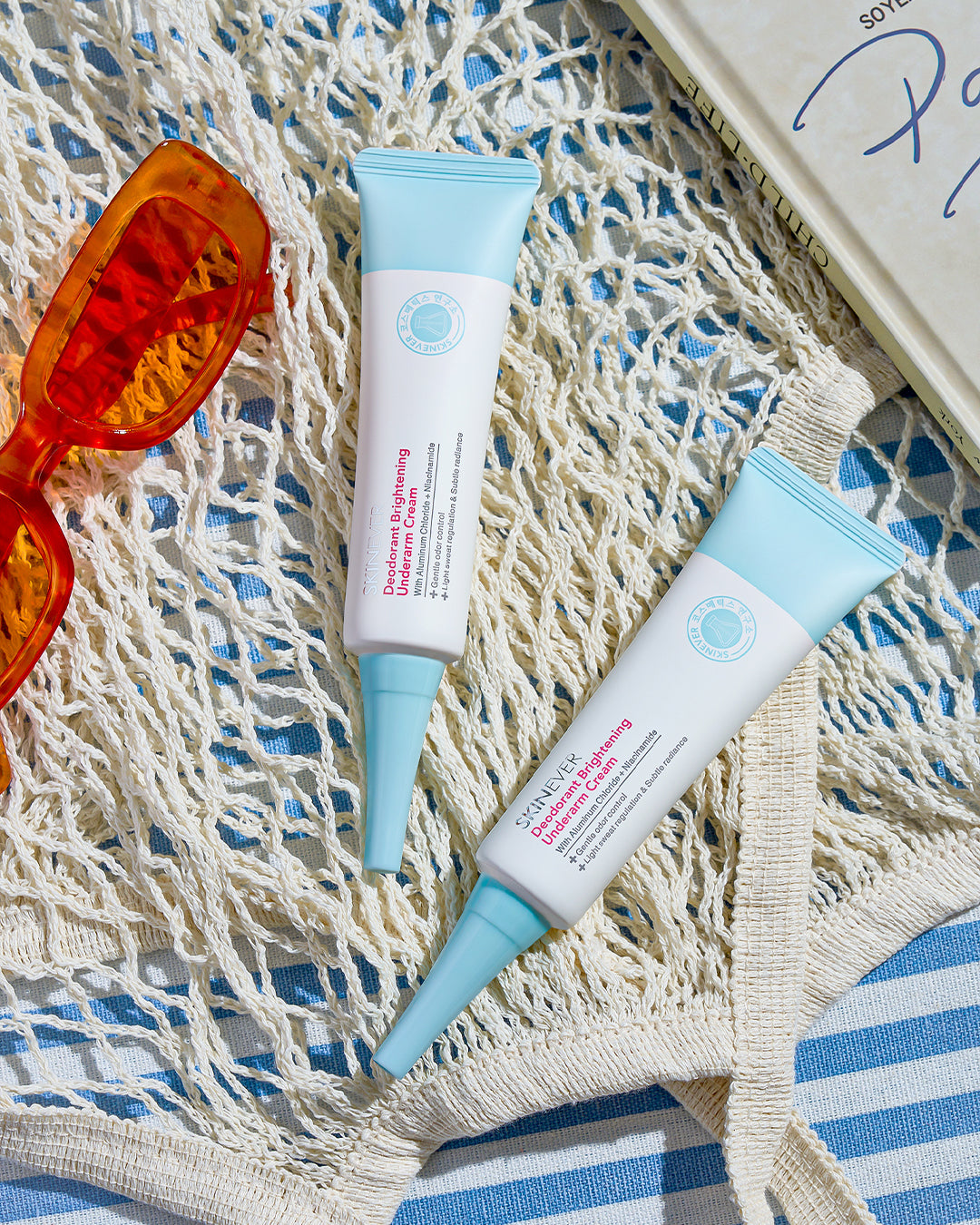 Two sunscreen bottles with blue pumps on a textured surface with sunglasses and a book.