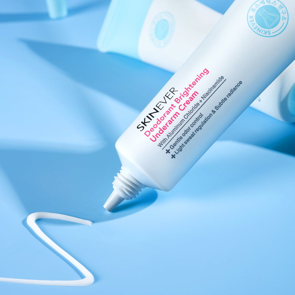 A close-up of a SKINEVER Deodorant Brightening Underarm Cream tube lying diagonally on a light blue surface, with a white smear of cream in the foreground and another blurred tube in the background.