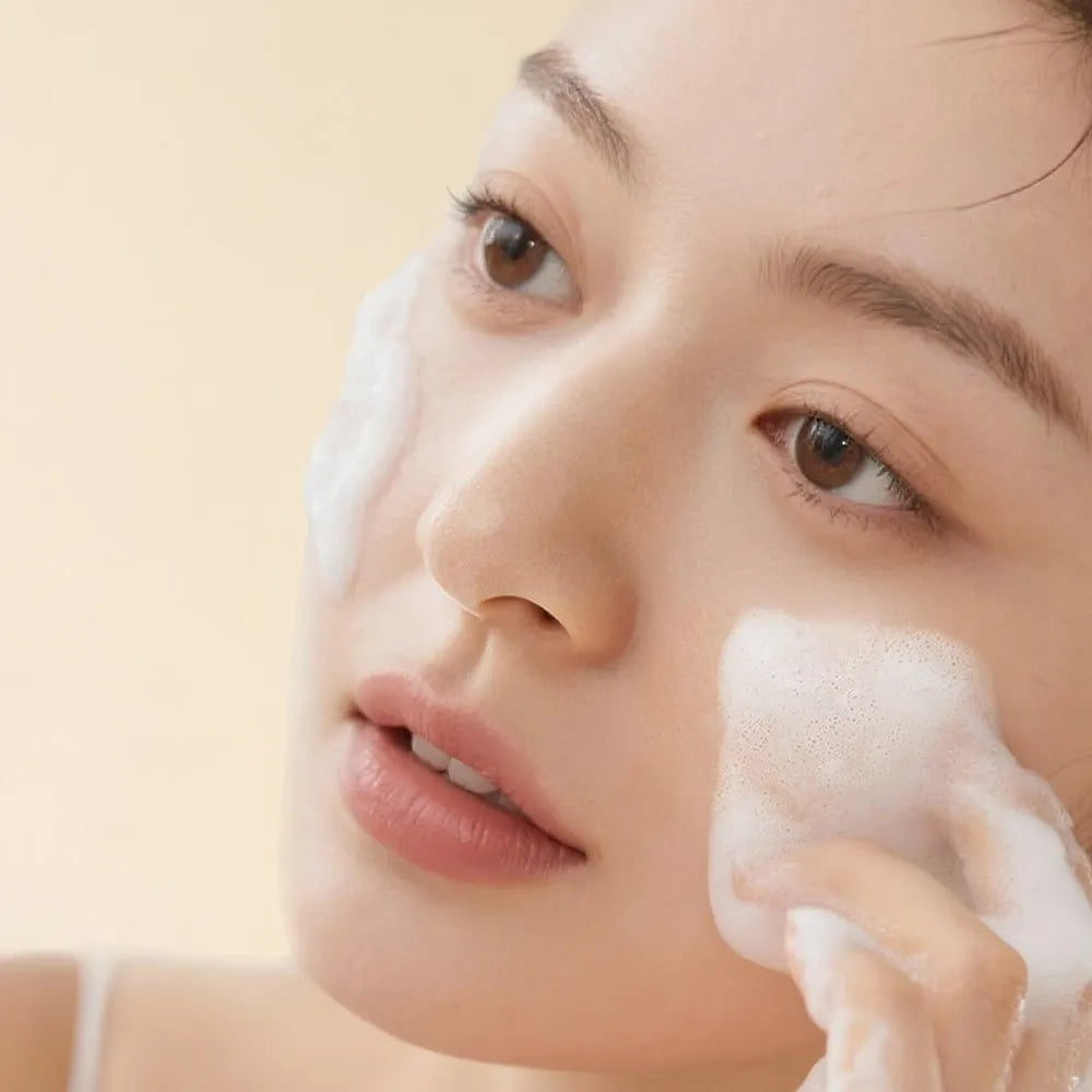 Woman applying a facial cleanser with a sponge on a beige background